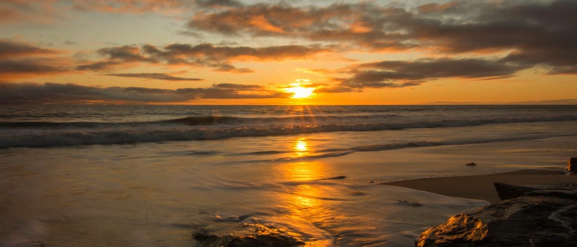 A quiet Tasmanian beach at sunset, the sun low over calm water and wet sand reflecting the sky