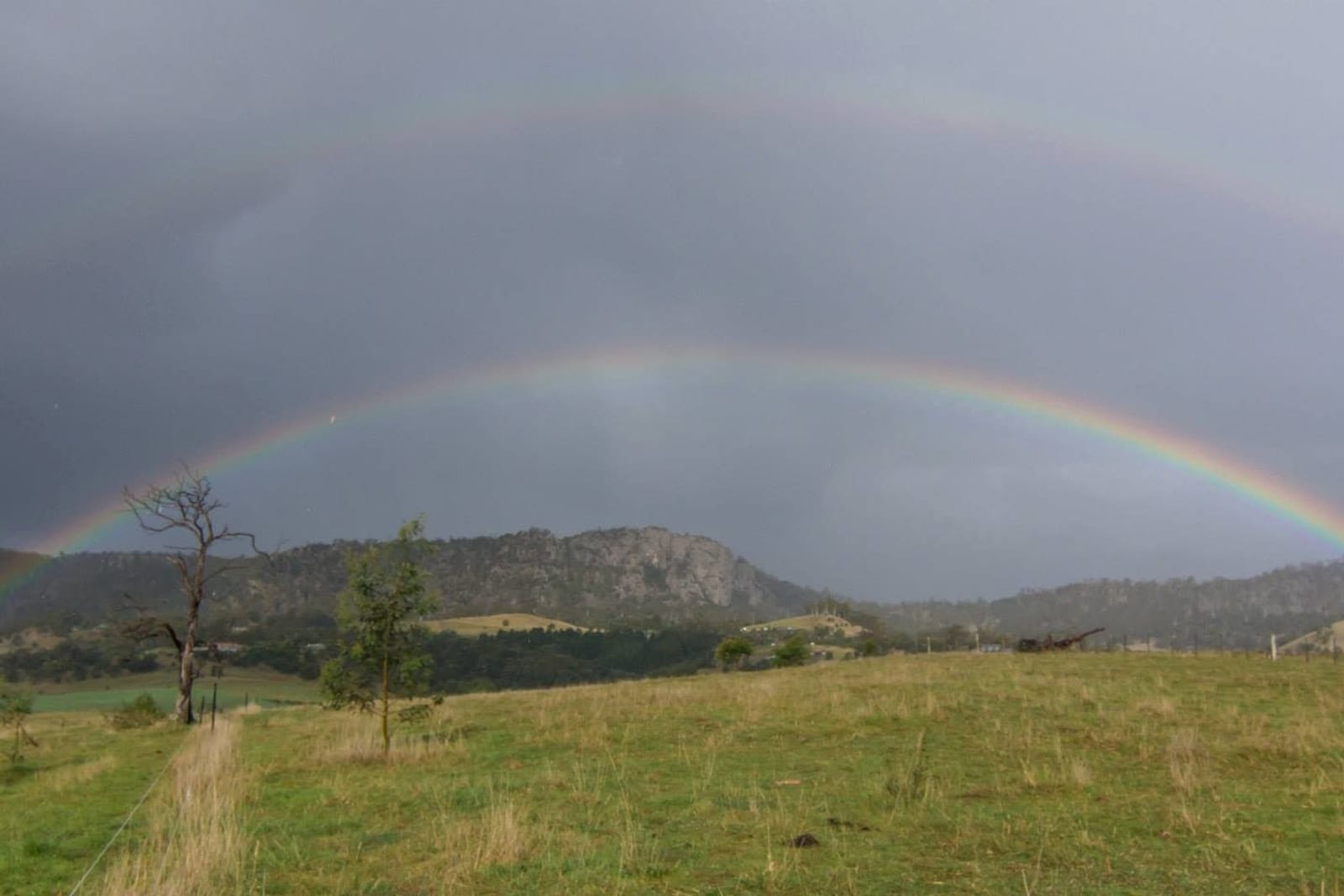 A double rainbow arcing over green Tasmanian farmland after rain